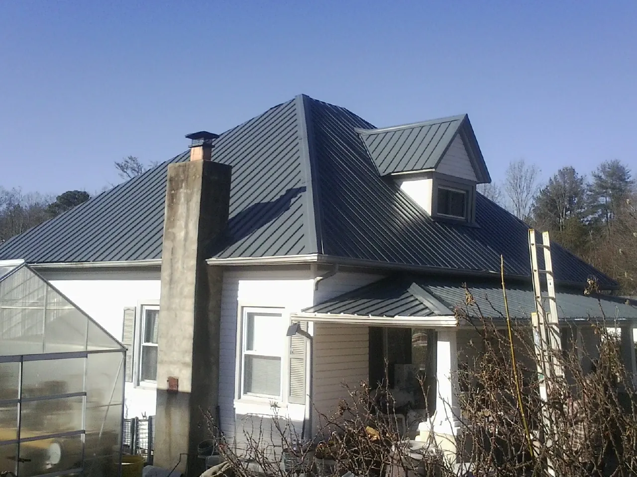 Dark blue standing seam metal roof on a white farmhouse with dormer — Slate & Tile Roof Repair by Roofing Brothers in Elwell