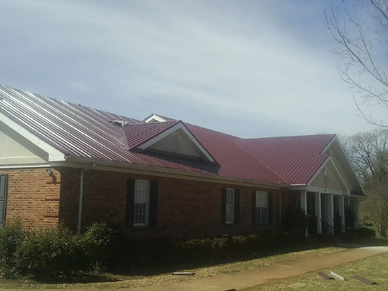 Red metal roof with gabled entries on a long brick building, from a Hail Damage Roof Repair job in Elwell