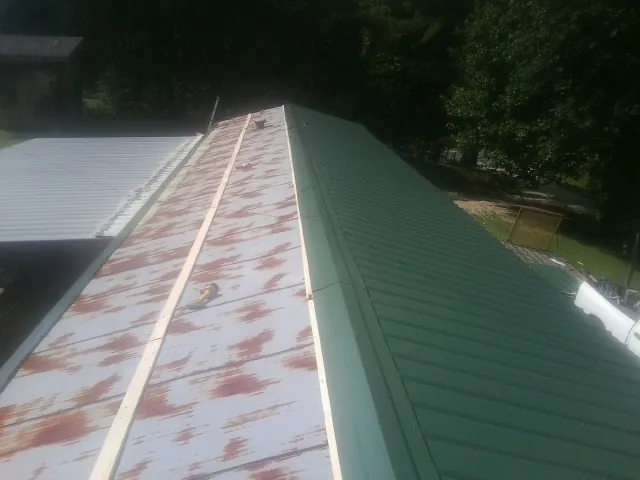 Old rusted panels beside newly installed green metal roofing — Wind Damage Roof Repair by Roofing Brothers in Elwell