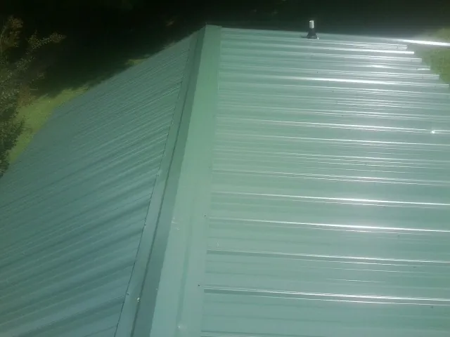 New green metal panels meeting at the ridge of a roof — Flat Roof Repair work by our crew in Elwell