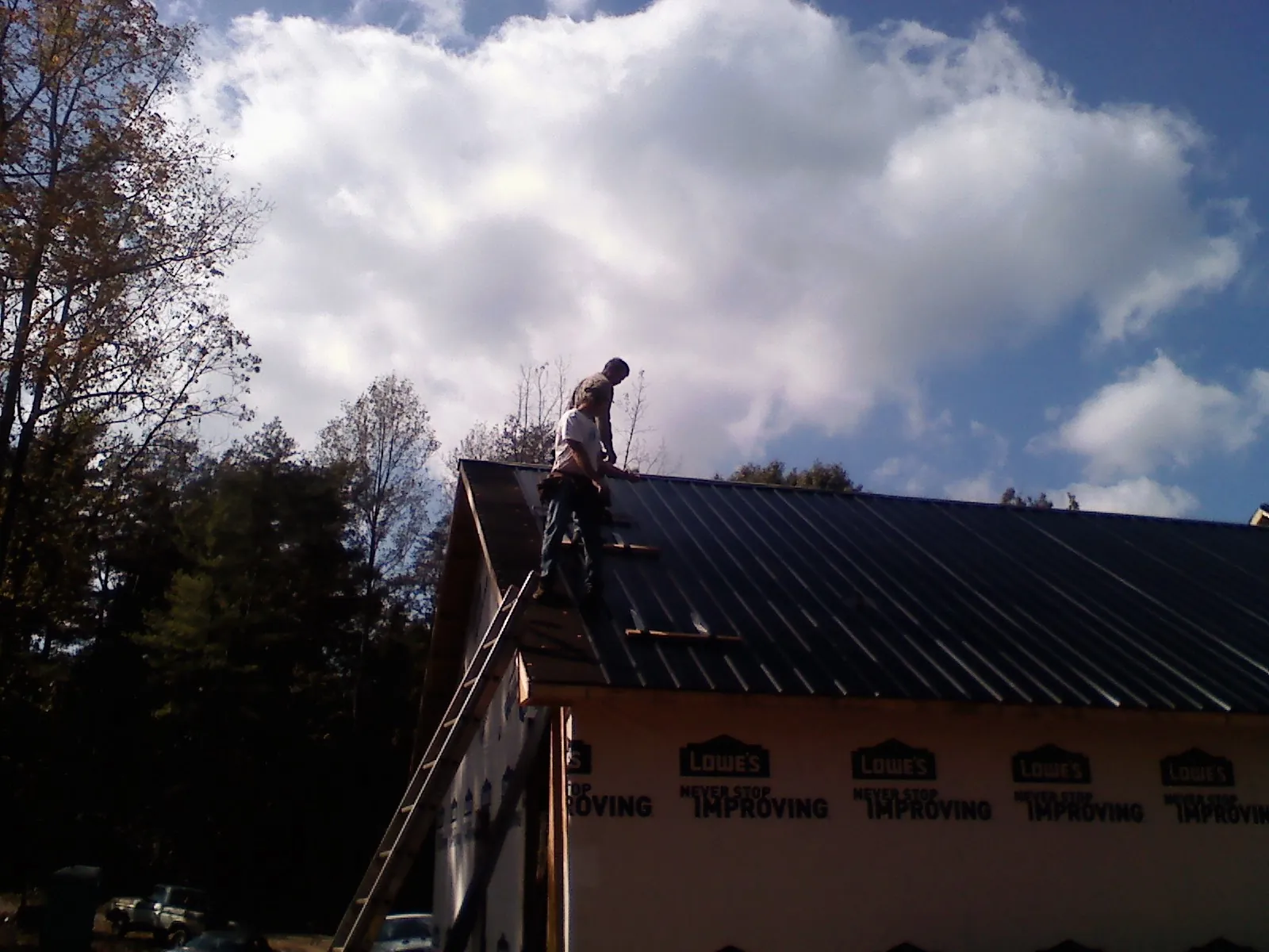 Roofer fastening dark metal panels high against a cloudy sky, from a Roof Inspection job in Elwell