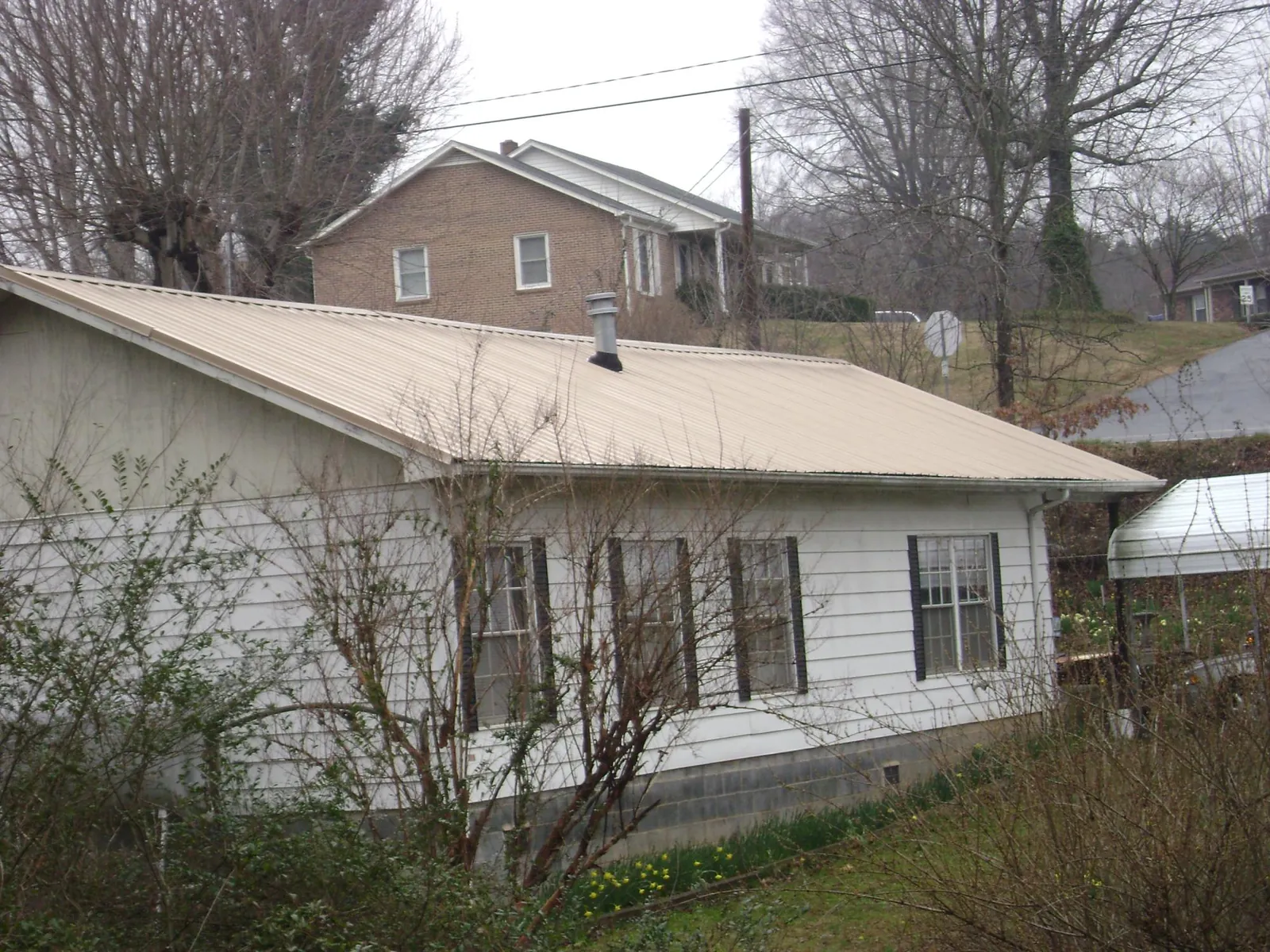 Tan metal roof on a white sided house set into a hillside — Commercial Roofing by Roofing Brothers in Elwell